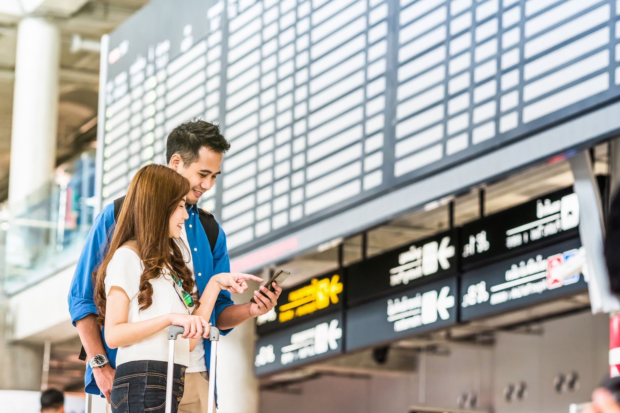Asian Couple Traveler Using The Smart Mobile Phone For Check In At The Flight Information